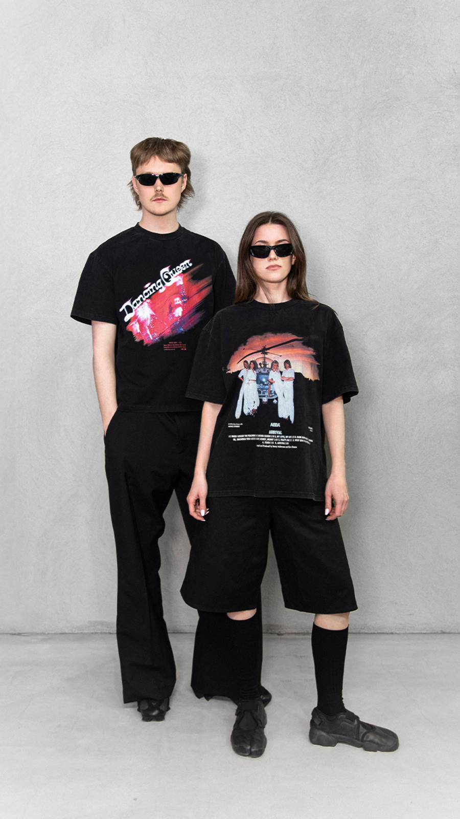 Two people wearing black graphic t-shirts and sunglasses on a plain background